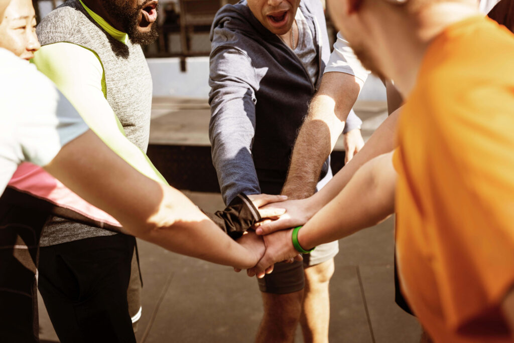 7 runners engaged in a team huddle, with arms extended and hands stacked in the middle — a suggestion for how to boost employee morale.