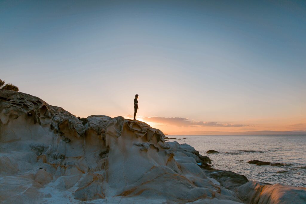 Person Standing on Rocks Overlooking Water